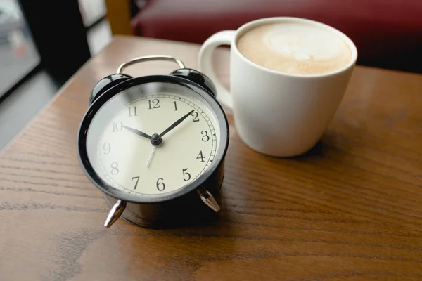 Чашка з кавою, поміщена поруч з будильником на дерев'яному столі — стокове фото