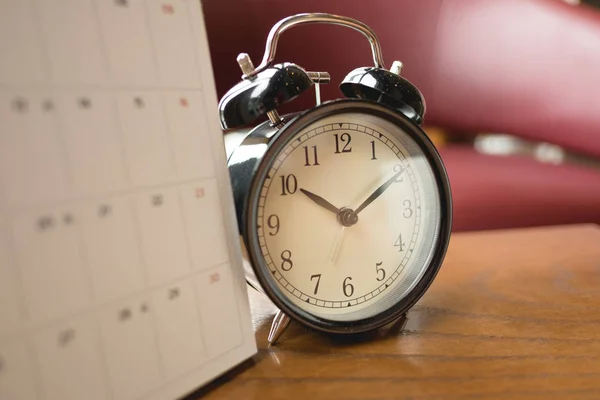 Reloj despertador colocado junto al calendario en la mesa de madera con ventana a —  Fotos de Stock