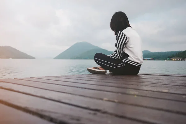 young woman sit alone on wooden bridge has river, mountain, sky