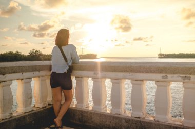 Geçmişe yolculuk yap. Gün batımında ve akşam denizinde tek başına duran genç kadına bak.