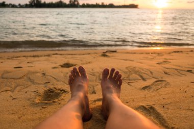 Sahilde genç bir kadının ayağıyla denizin güzel günbatımı.  