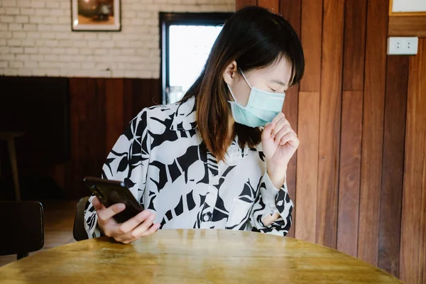 caucasian woman sick wearing masks her holding mobile phone and look like symptom coughing while at home. image for social distinction, portrait, covid-19, healthy, person, and corona virus