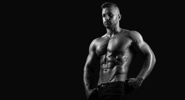 Young handsome, strong muscular male fitness model / bodybuilder with drops of water on shiny skin poses on isolated black background showing his perfect abs high contrast beautiful image