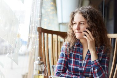 Genç sevimli kadın yalnız serbest zaman sırasında kafede otururken cep telefon arıyor. Şüpheli ve kararsız pencerede düşünceli düşünceli ifade ile onun öğle yemeği için hazır olmak bekleyen onun dudakları pursing bakıyor.  
