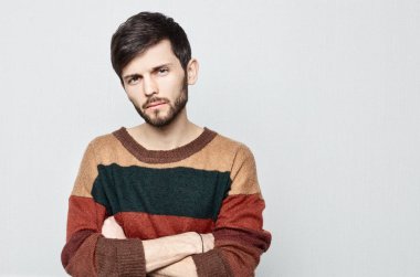 Genç sakallı hippi erkek seyir stüdyo portre üzgün, kayıtsız, utanç verici ve kaba. Eski moda renkli kazak adam haç kolları ve bakışları hoşnutsuzluğunu içinde giyinmiş.