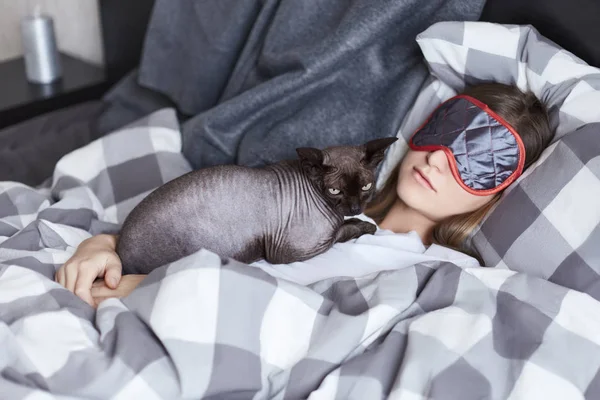 Два друга кот-сфинкс и юная леди, оба в фокусе. Девочка спит в постели, прячется от дневного света в маске для глаз. Ее кошка отдыхает в груди. Отдохните, расслабьтесь, расслабьтесь. . — стоковое фото