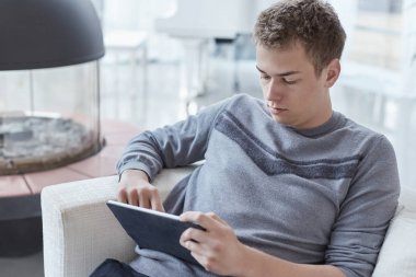 Çekici genç kafkas erkek evde tablet, işten sonra beyaz koltukta tek başına oturan ile rahatlatıcı. Genç hippi kız online app onun modern gadget'ı kullanarak, görüntülü görüşme sahip.