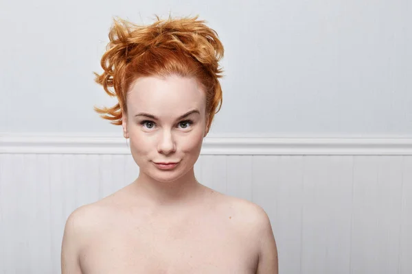 Close up of redhead young Caucasian woman with freckles wearing nothing looking at the camera with serious and concentrated expression waiting for the answer or an action from her boyfriend. Human emotions concept.