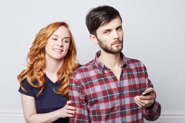 İnsan ve teknoloji. Mutlu çift birlikte cep telefonu kullanma. Kızıl saç ve sakallı ciddi arkadaşının elektronik cihazın ekranına bakarak sevimli gülümseme ile güzel bir kız. İnsan duygu ve ifadeler. 