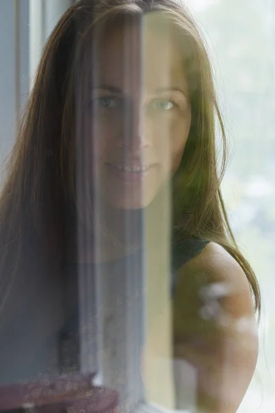 Крупным планом портрет счастливой белой женщины с голубыми глазами, улыбающейся и смотрящей вперед жестко стекло окна  . — стоковое фото