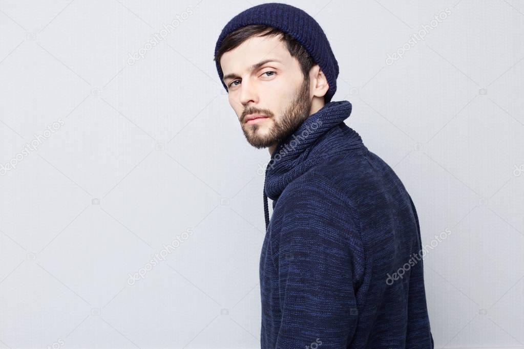 Sideways portrait of natural brunette Caucasian man wearing warm clothes on white background. Bearded hipster with clean shaved temples and stylish well-trimmed mustache looking serious and brutal at the camera.