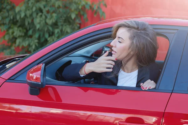 Retrato de la joven atractiva dama de negocios caucásica con el pelo largo que lleva traje formal en la rueda de coche moderno rojo mirando a lo lejos esperando a su jefe para venir a la oficina. Imagen en movimiento . — Foto de Stock