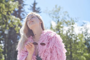 Açık havada beyaz duvarlı içten gülümseme ile aşk hakkında rüya romantik Tarih için bekleyen güneş gözlüğü tutan şehir parkında duran pembe funky palto giyiyor yakışıklı sarışın beyaz kadın