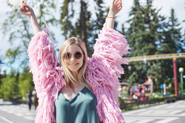 Foto ravvicinata di una giovane studentessa caucasica vestita di rosa, che sorride alla telecamera con espressione allegra, sogna e gode del caldo vento estivo, ride e balla da sola con le mani in alto . — Foto Stock