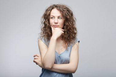 Şüpheli ifade sahip, uzakta kurnazca kararsızlık içinde seyir, çenesinin tutarak, en iyi çözüm bulmaya güzel raslantı giyimli genç beyaz bir kadın portresi. Beden dili kavramı.