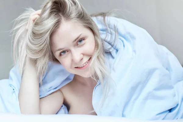 Nabídka portrét krásné dámy kavkazské, pózuje se šťastným úsměvem v posteli ráno. Mladá atraktivní blue eyed žena má dlouhé blond vlasy hravě při pohledu na fotoaparát. Koncept zdraví a krásy. — Stock fotografie