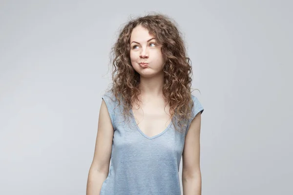 Headshot του δυσαρεστήθηκε Ευρωπαία γυναίκα ανατίναξη της μάγουλα είναι αναστατωμένος αύξηση τα φρύδια, αποδεικνύοντας τη δυσαρέσκεια. Γυναίκες σε γκρι t-shirt με σκυθρωπός έκφραση που απομονώνονται σε λευκό φόντο — Φωτογραφία Αρχείου