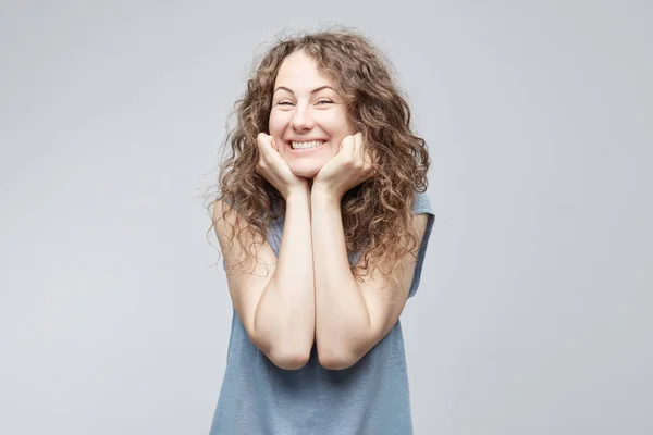 Retrato de mujer europea contenta de pelo rizado mirando con sus ojos azules cálidos y sonrisa de diente salido con mirada sincera y gentil cogidas de la mano bajo la barbilla. Gente, belleza, concepto de emociones . —  Fotos de Stock