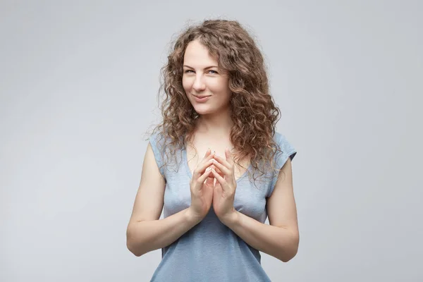 Retrato de una atractiva dama mirando astuta y misteriosamente a la cámara sosteniendo juntos a Hans teniendo algunas ideas en su mente. Hembra de pelo rizado con ojos azules que concibe algo con mirada juguetona . —  Fotos de Stock