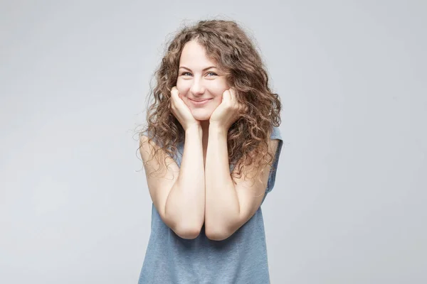 Retrato de mujer europea contenta de pelo rizado mirando con sus ojos azules cálidos y sonrisa salida con mirada sincera y suave cogida de la mano bajo la barbilla. Gente, belleza, concepto de emociones . —  Fotos de Stock