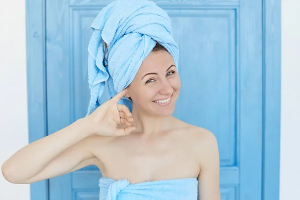 Youth, happiness, people and lifestyle concept. Indoor shot of attractive joyful young European woman with blue towel bun, smiling widely, cleaning her ears after taking a shower, looking playfully