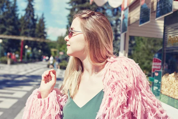 Nära upp skott av unga blonda hipster student bär funky rosa jacka, leende, blundar med glada ansikte uttryck, drömmer, njuter av varm sommar vind medan väntar popcorn i nöjesparken. — Stockfoto