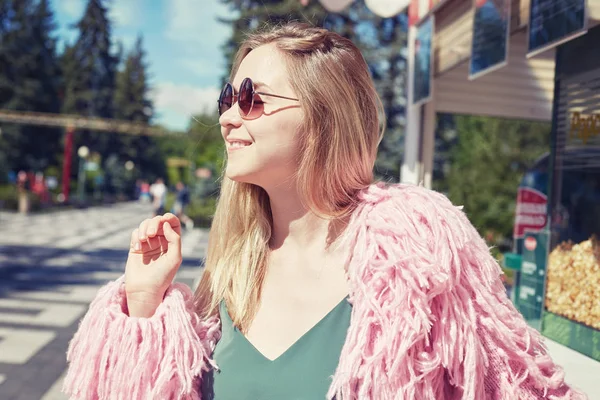 Nära upp skott av unga blonda hipster student bär funky rosa jacka, leende och stänga hennes ögon med glada ansikte uttryck, drömmer och njuter av varm sommar vind medan promenader utomhus ensam. — Stockfoto