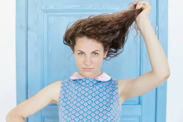 Concetto gioventù e felicità. Vista da vicino della bella donna dagli occhi azzurri caucasici, guardando la fotocamera, giocando con i suoi lunghi capelli ricci ricci. Giovane signora tenera con perfetta pelle bianca sana . — Foto Stock