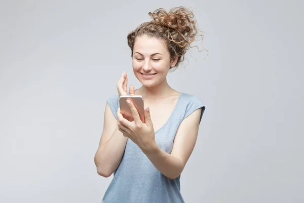 Retrato de estudio de mujer bonita con peinado rizado, disfrutando de la comunicación en línea en el teléfono móvil genérico, mensajes de texto amigos a través de mensajeros. Personas, estilo de vida, tecnología y aparatos electrónicos modernos . —  Fotos de Stock