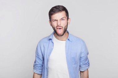 Duygusal ve sakallı genç yakışıklı esmer adam çalışan yapması, ağız yapma, kamera birisi, küçük yaramaz çocuk gibi davranmayı takılmaya çalışıyorum, dili dışarı yapışmasını mavi gömlek giymiş.