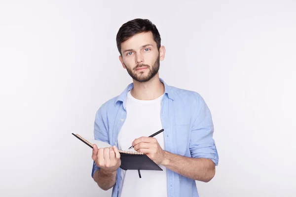 Foto de estudio de un hombre de negocios barbudo europeo o estudiante vestido casual, escribiendo notas en su cuaderno mientras estaba de pie aislado sobre un fondo blanco, mirando seriamente a la cámara. Personas, negocios, carrera . — Foto de Stock