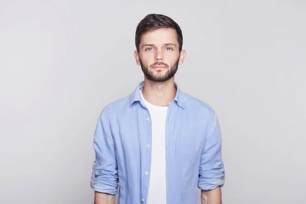 Retrato de branco bonito morena cara com olhos azuis, penteado da moda e barba olhando seriamente para a câmera enquanto posando contra a parede do estúdio branco. Empresário sério de camisa a pensar no trabalho . — Fotografia de Stock