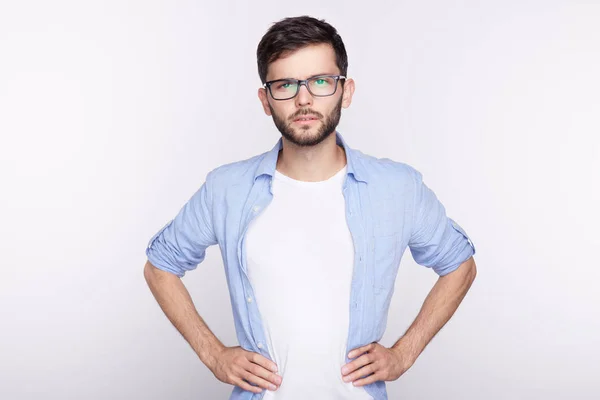 Imagen de una atractiva estudiante caucásica seria con barba pequeña y bigote, vestida con una camiseta casual, mirando a la cámara con expresión facial confiada y reflexiva de pie en la pared blanca . — Foto de Stock