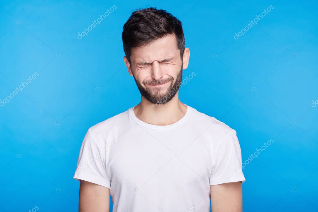 Close-up of childish Caucasian student male with brunette hair blowing his cheeks bursting out laughing having joy squinting. Lucky male amazing himself. Positive body language emotions and feelings.