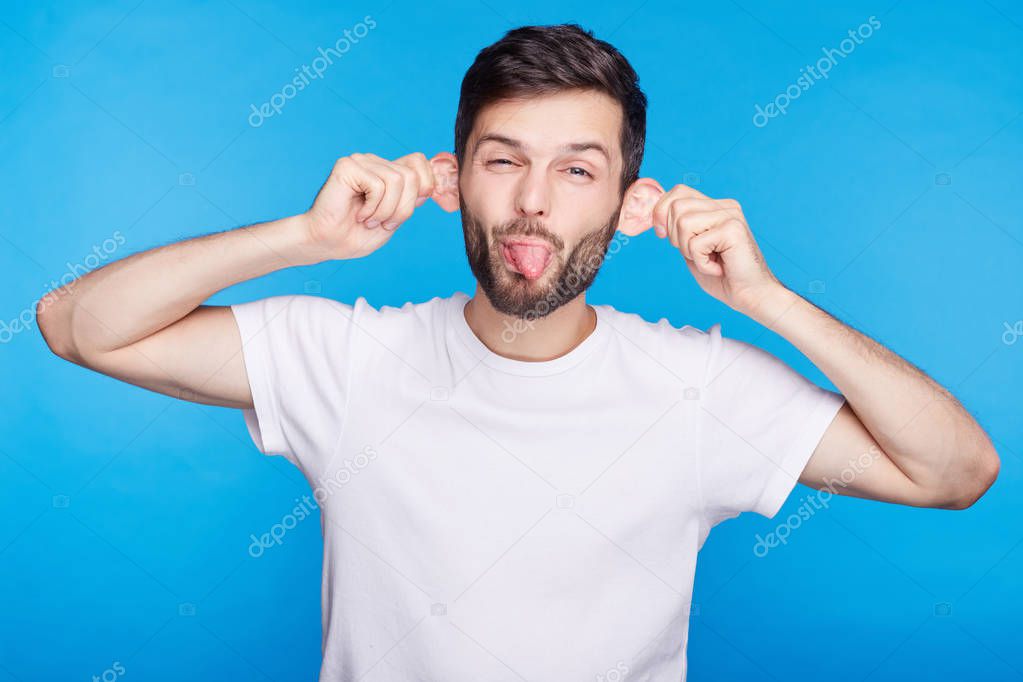 Funny young Caucasian man grimacing making mouths, sticking out his tongue at camera, making ears stick out while trying to make his crying baby laugh, having stupid and ridiculous facial expression.