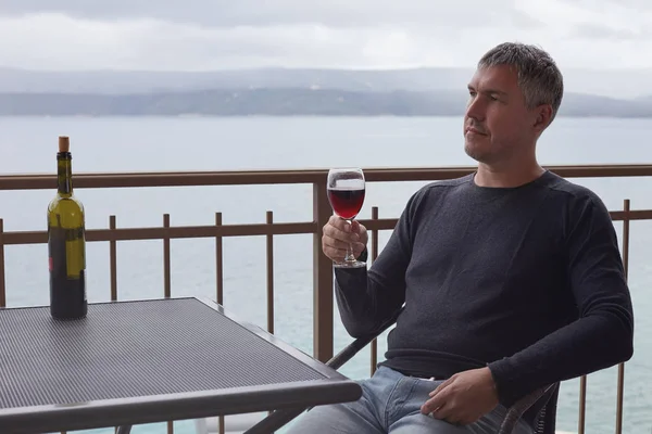 Портрет зрілих кавказьких красенем насолоджуючись його свято, що пити червоне вино, тільки в другій половині дня. Чоловік дивиться далеких, милуючись мальовничими пейзажами хмарно літній день сидячи на балконі. — стокове фото