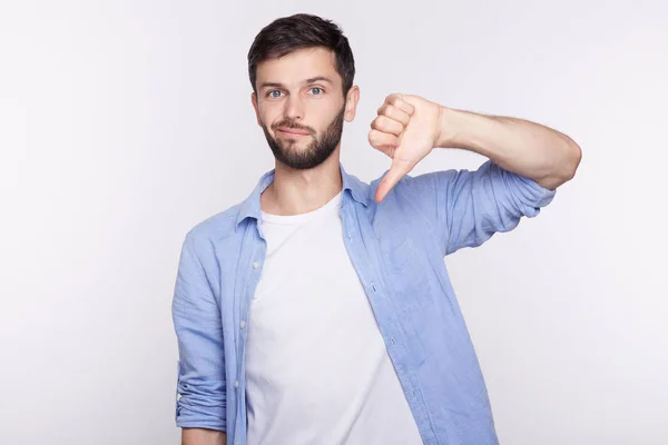 Retrato de estudio del hombre hipster barbudo mirando a la cámara con ropa casual elegante expresando disgusto, desaprobación, falta de respeto o desprecio con gestos, mostrando pulgares hacia abajo y muecas . — Foto de Stock