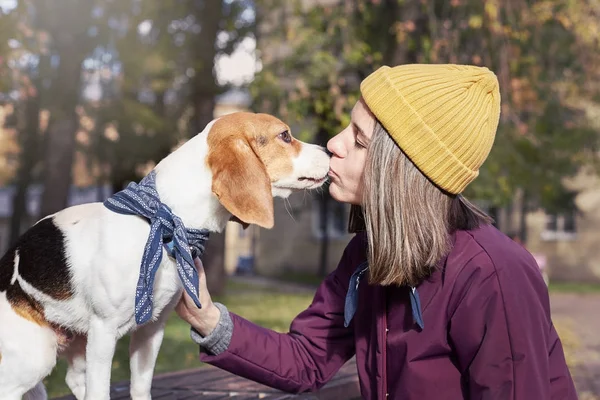 Ritratto ravvicinato di hipster giovane donna caucasica bacia il suo cucciolo beagle. Colpo all'aperto di signora e il suo animale domestico godendo di bel tempo autunnale. Emozioni umane positive, espressione facciale, concetto di sentimenti . — Foto Stock