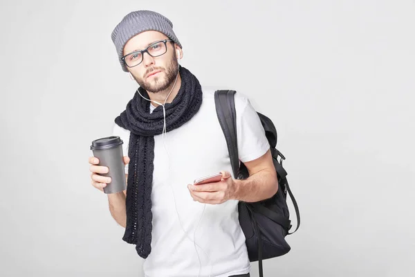 Hombre guapo en gafas de sol de moda sosteniendo taza de café disfrutando de su lista de reproducción de comprobación de sabor en el teléfono. turista de moda en sombrero gris de pie aislado beber té caliente que descansa después de un largo paseo . — Foto de Stock