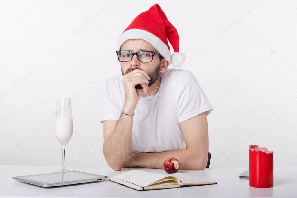 Handsome guy in red hat celebrates New Year alone at office due to circumstances. All he has is milk at fridge and apple. Sad and lonely young Caucasian businessman spending Christmas Eve in bad mood