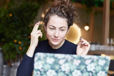 Avrupa kadın kıvırcık kilitler ellerini tutar, düz saçlara sahip olmak istiyor, acele modern Café özel toplantı yapmak için hangi saç modeli haberi yok. Bayan bir ayna gibi laptop monitör kullanır.