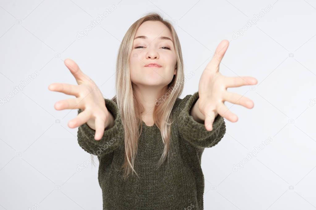 Adorable Caucasian blonde woman looking with great disbelief directly into camera, keeping arms wide open while being surprised with lovely present of her boyfriend, sending kiss ans hugs to lover.