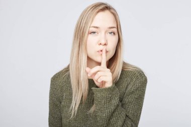 Güzel sarışın kadın yatay atış rahat yeşil Kazak giyer, sus işareti gösterir, ciddi ifadesi olan, sır Kimseye söylememem için en iyi ya da yakın arkadaşı sorar, sadakat ve sessizlik için umut.