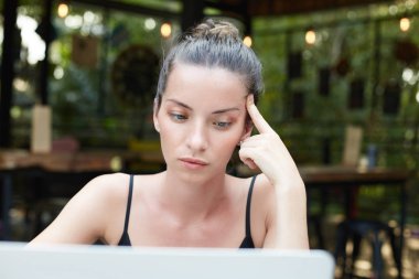 Güzel karışık yarış esmer kadınla iyi şekilli kaşları, yeşil gözleri ve tapınak düşünceli dokunuyor, laptop ile çalışan modern kafede oturan topuz saç sahip dolgun dudaklar parlayan portresi.