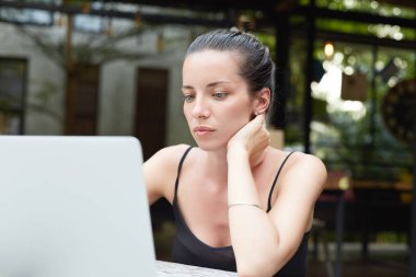 Kadın metin yazarı kırpılmış görüntü dizüstü organik yeşil arka plana sahip modern kafede uzaktan çalışır. Ciddi konsantre Bayan dikkatle görünüyor dizüstü bilgisayar, internet sitelerinde kitaplar.