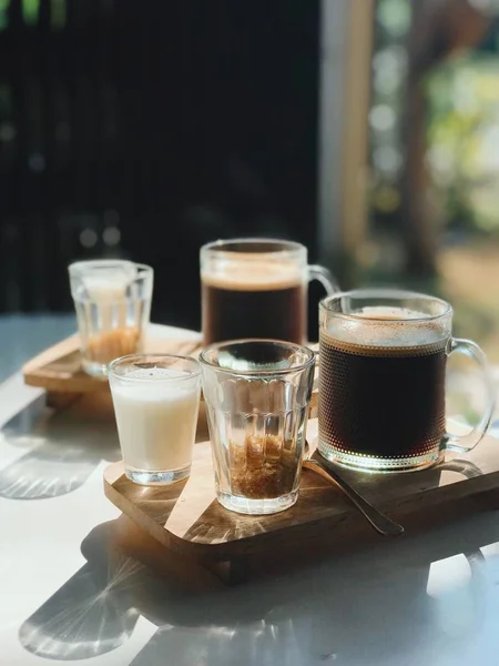Coffee set for two. Close up shot of beautiful served Americano long coffee with milk and brown sugar on a wooden plate. Fresh morning breakfast on sun rays.