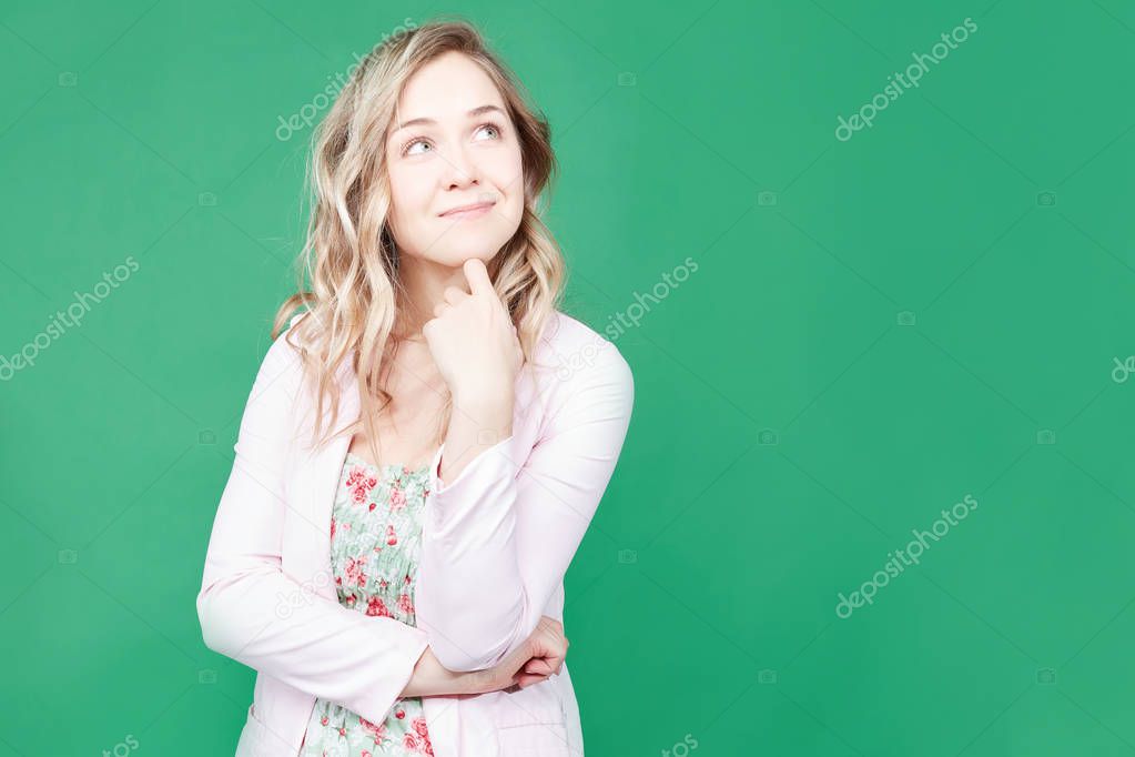 Adorable thoughtful blonde woman looks upwards, poses against green background with copy space for your promotional text or advertisement. Pensive pretty female ponders about something in life.