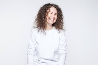 Beyaz boş duvara poz casual beyaz T-shirt giyen olumlu erkek çekici görünüm ile gülümseyen. Mutlu kadın kıvırcık saçlı hoş iltifat aldıktan sonra olumlu duygular gösterilen.