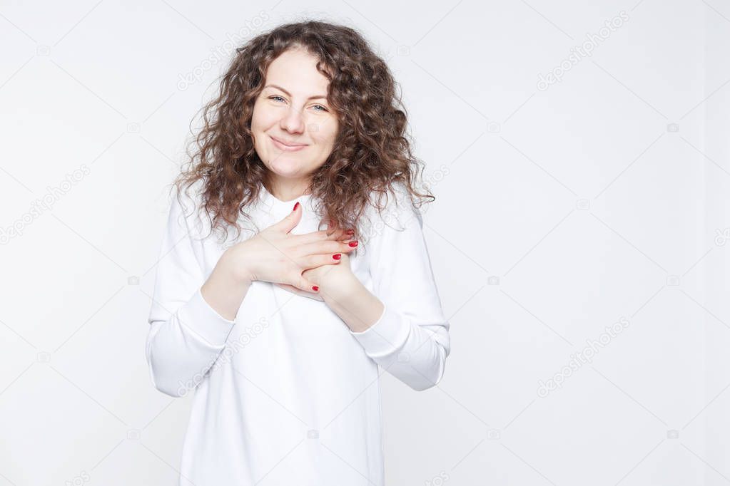 Kind pleasant looking good natured female with appealing appearance looks with pleased expression into camera, keeps hands on heart, expresses positive feelings towards boyfriend, isolated on white.