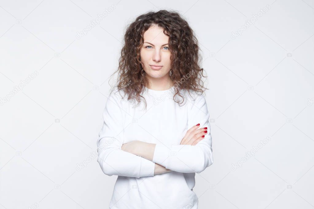 European beautiful woman dressed casually, keeps hands crossed, spends free time at home alone, poses at camera, isolated over white studio background. People, youth, relationship, beauty concept.